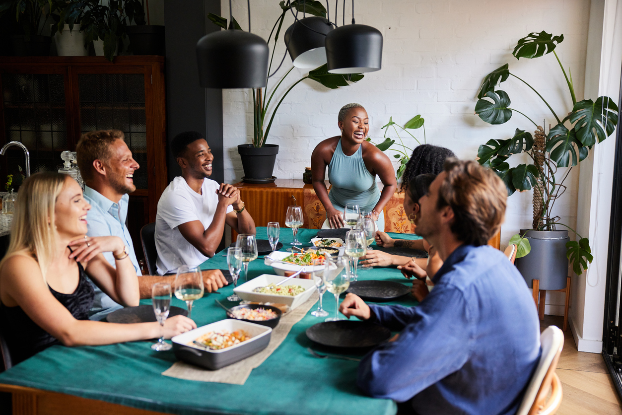 A group of friends sitting around a table at a dinner party while their host begins to serve food