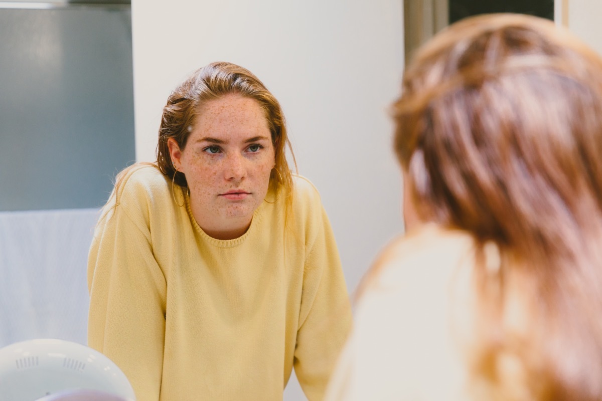 A depressed teen helplessly stares at her reflection in the bathroom mirror.