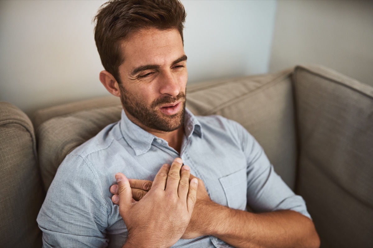 Shot of an uncomfortable looking young man holding his chest in discomfort while being seated on a couch at home