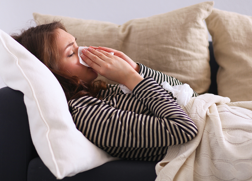 woman sneezing sick on the couch