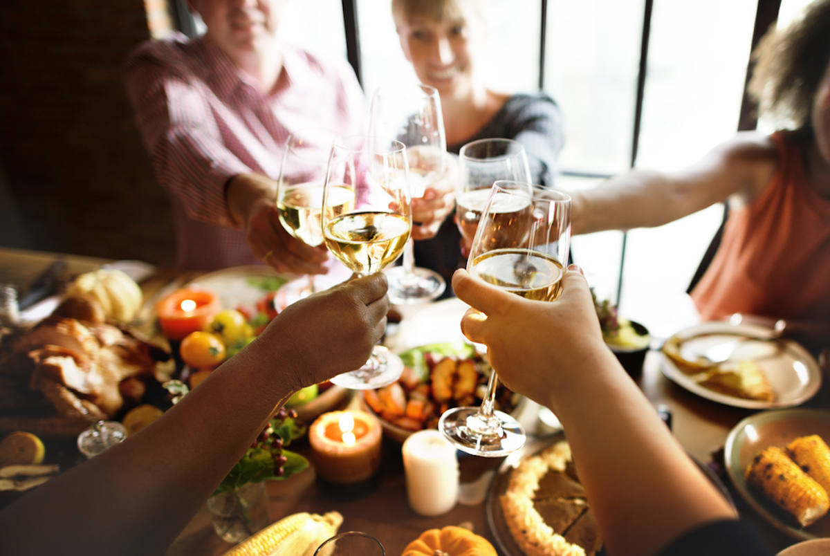 closeup of hands clanking wine glasses over thanksgiving table