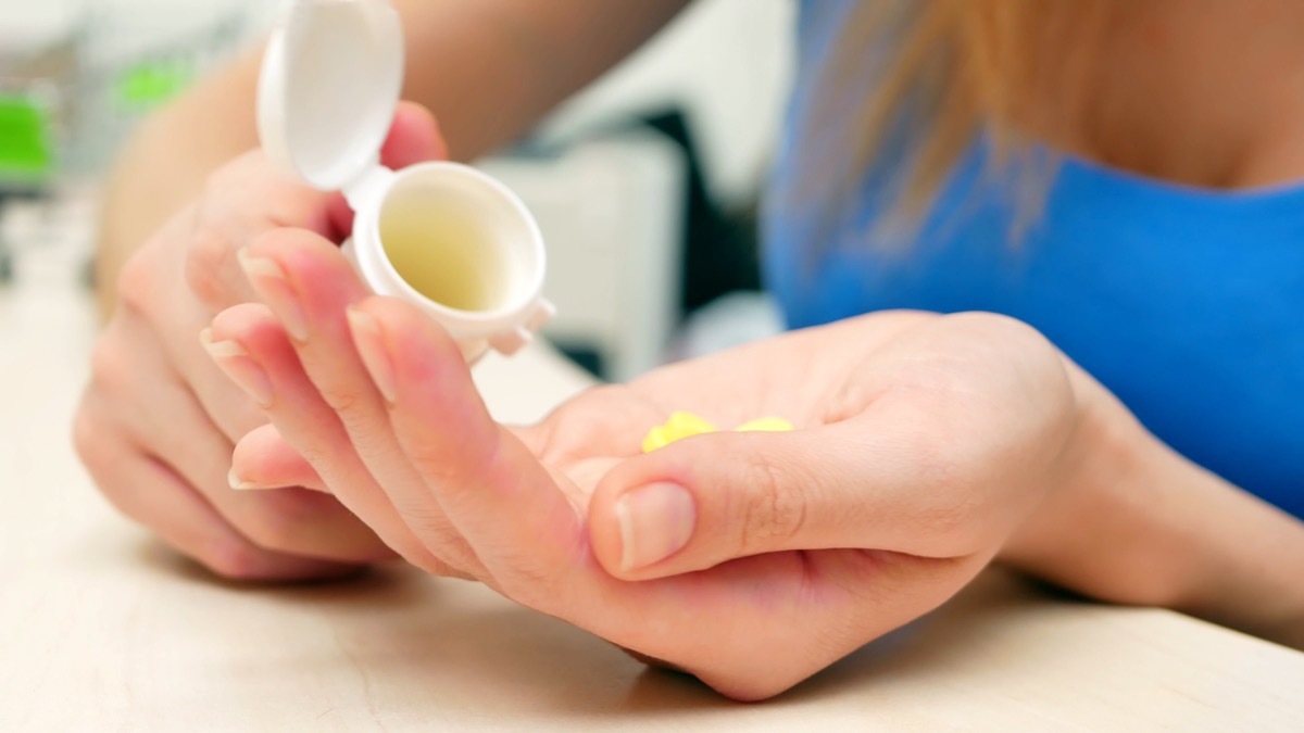 woman in blue shirt pouring supplements in white bottle into hand