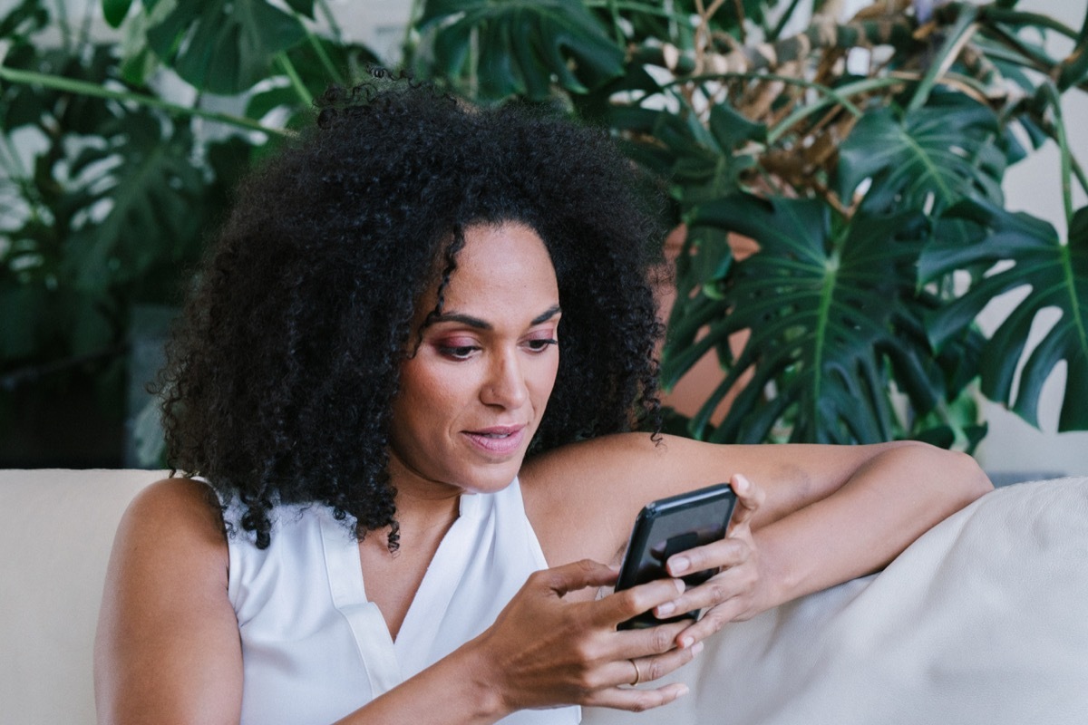 serious woman sitting on a sofa texting someone