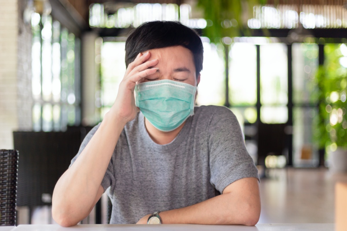 asian man wearing a mask has a headache