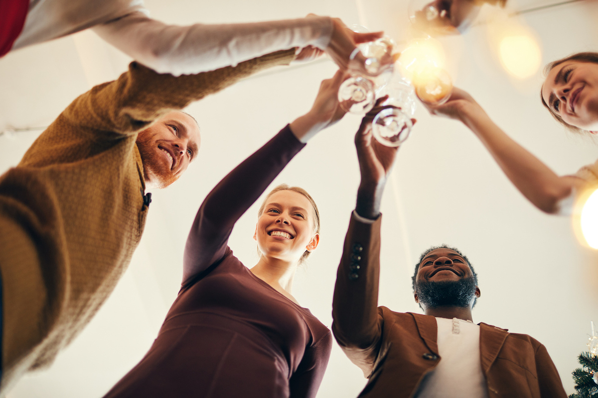 Low angle view at multi-ethnic group of people e clinking champagne glasses at an indoor gathering