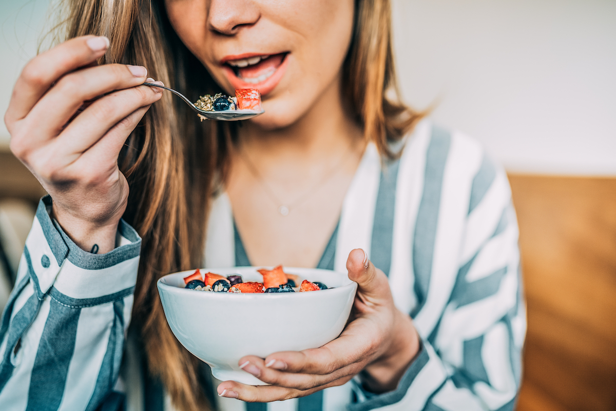 close up of woman eating oat and fruit in bowl for breakfast