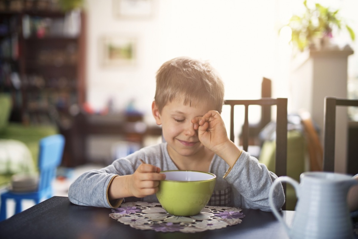 tired boy eating cereal in the morning