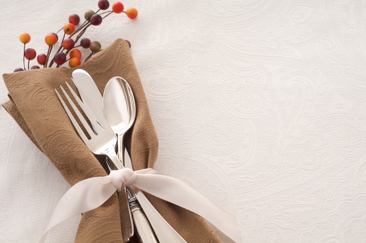 Antique Silverware Place Setting in a Brown Napkin and Tied with Ribbon on White Backgroun