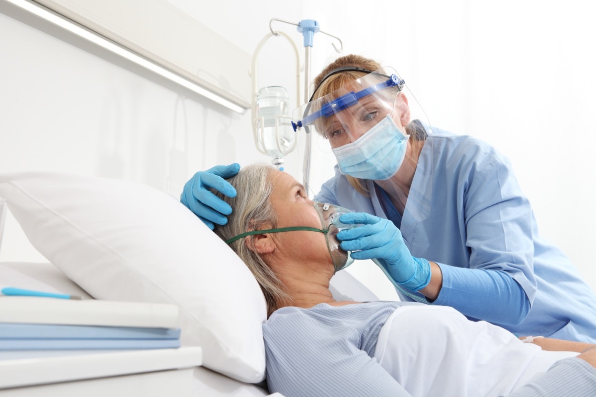 A nurse puts oxygen mask on elderly woman patient lying in the hospital room bed.