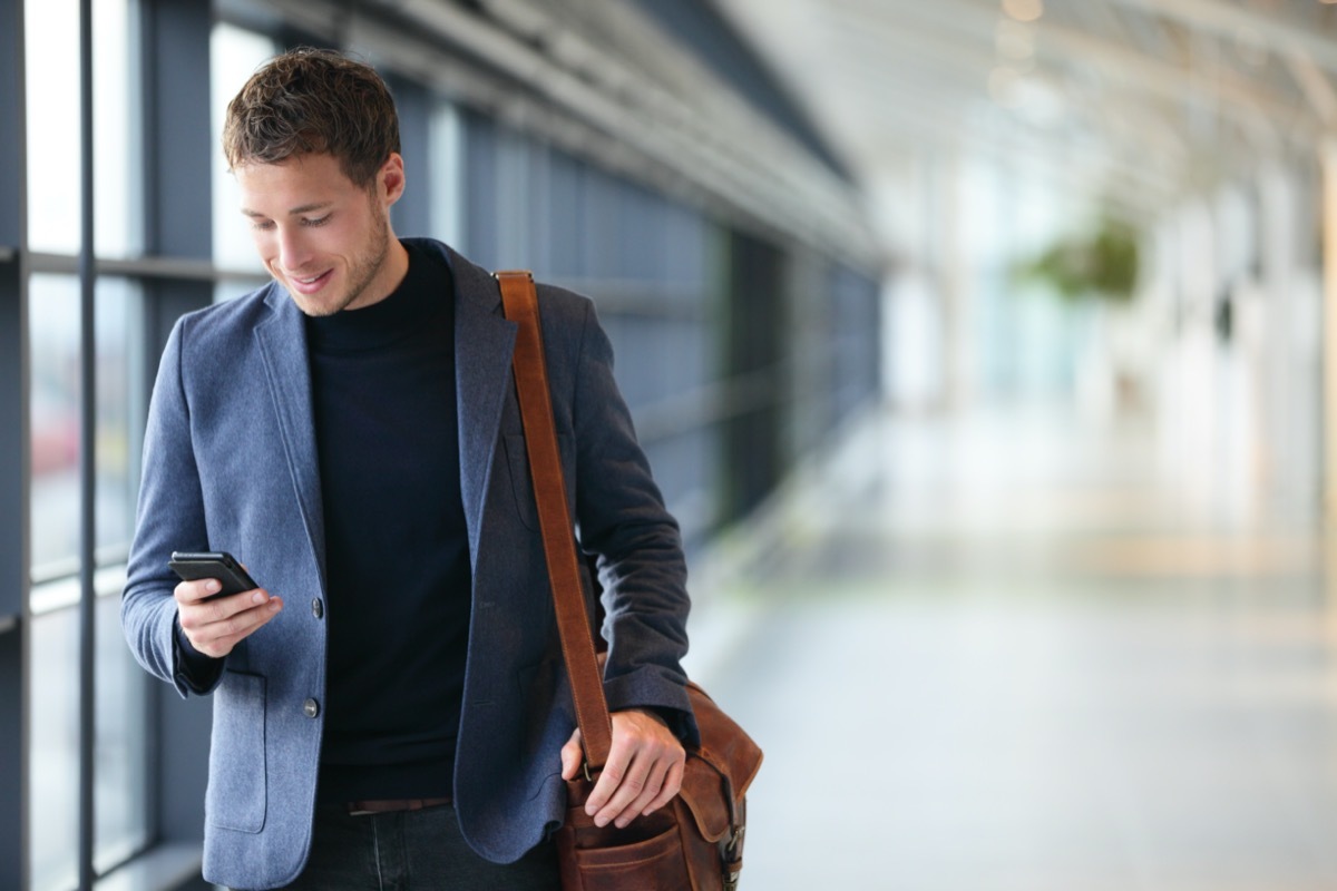 Man on smart phone - young business man in airport. Casual urban professional businessman using smartphone smiling happy inside office building or airport. Handsome man wearing suit jacket indoors.