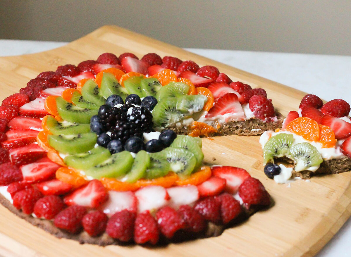 Slicing up a sugar cookie fruit pizza on a wooden pizza pan