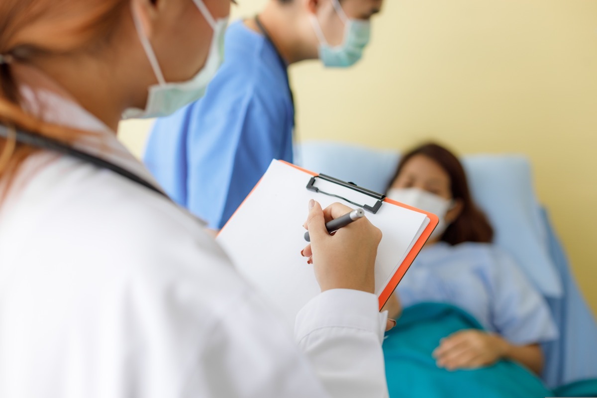 Female and male doctors wearing masks and uniforms are visiting to check the symptoms of middle-aged female patients lying in bed.