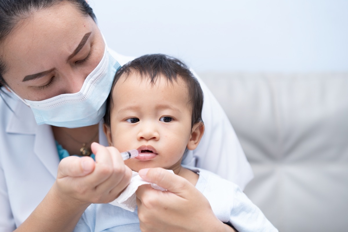 woman administering liquid medicine to young boy