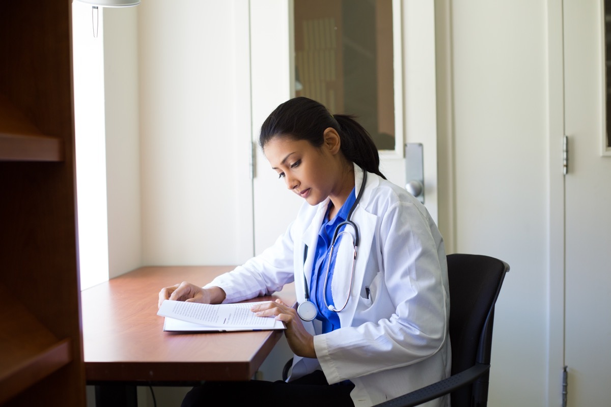 Closeup portrait, woman healthcare professional with stethoscope enjoying reading, studying in library room - Image