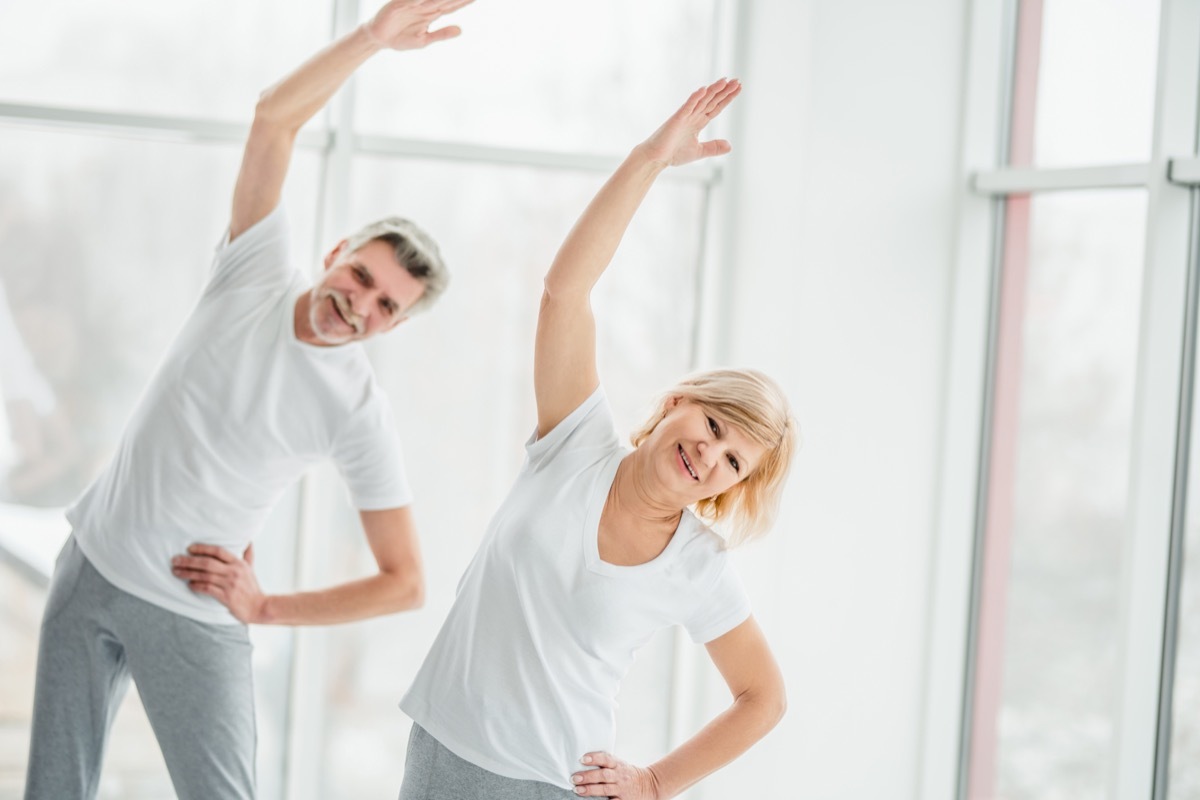 Beautiful senior couple doing fitness training together in the white gym with panoramic windows. Health and sport concept.