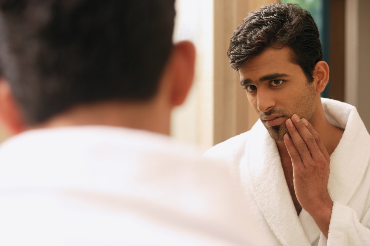 young man inspecting face in mirror