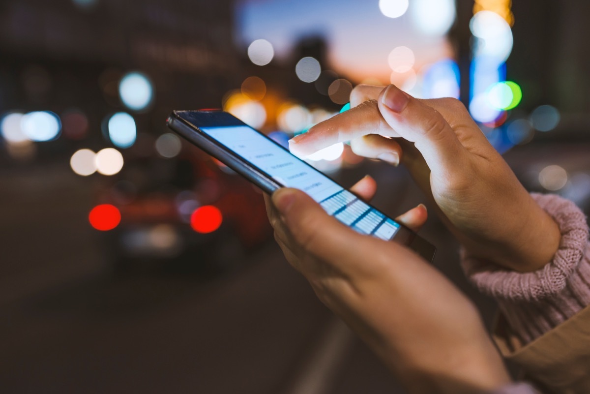 Girl pointing finger on screen smartphone on background illumination bokeh color light in night atmospheric city, using in hands texting mobile phone. Using cellphone at night