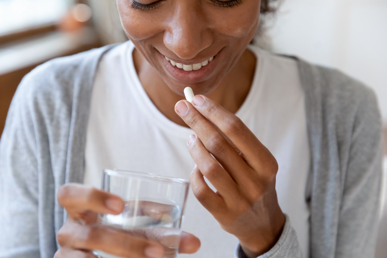 A young woman taking a supplement pill with a glass of water