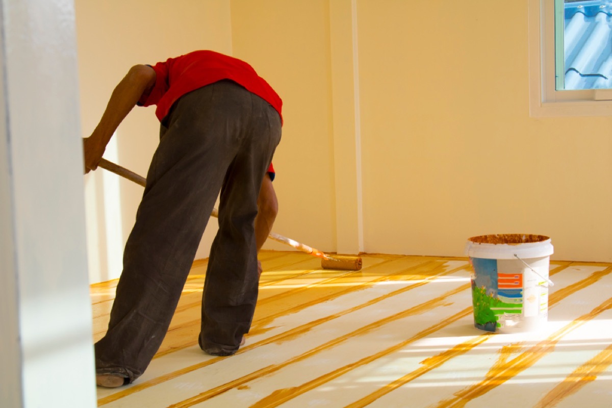 man in red shirt and black pants painting wood floors yellow