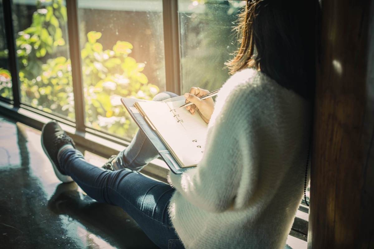 woman sitting in a cafe writing new years resolutions in a journal