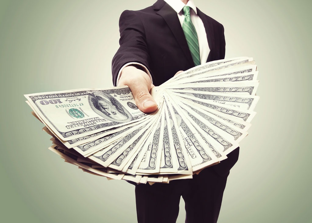 man in suit holding a fanned out stack of dollar bills to the camera