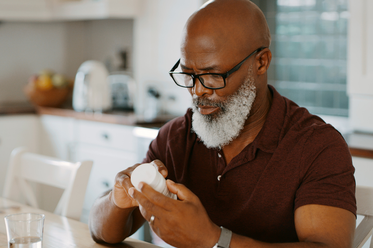 senior man sitting alone in his kitchen and taking pills