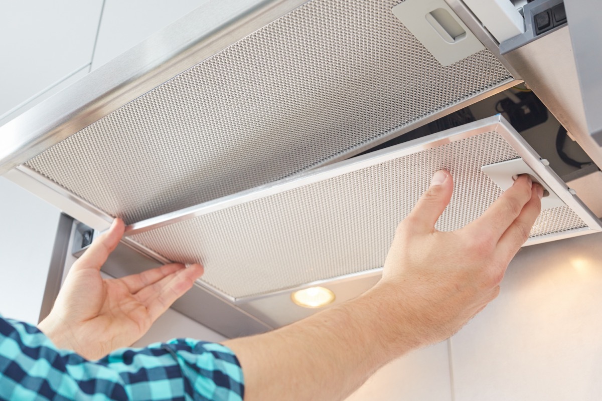 two hands cleaning range hood over stove