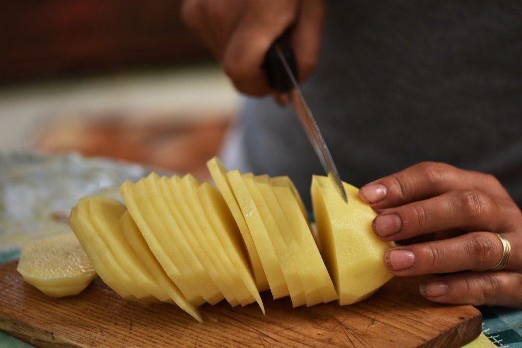 a man slicing a peeled potato