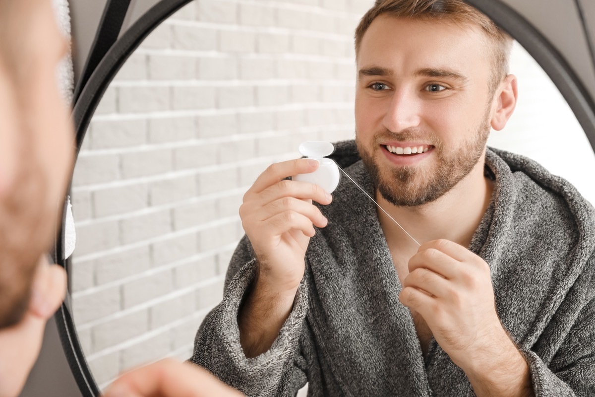 Man in a robe flossing in the mirror