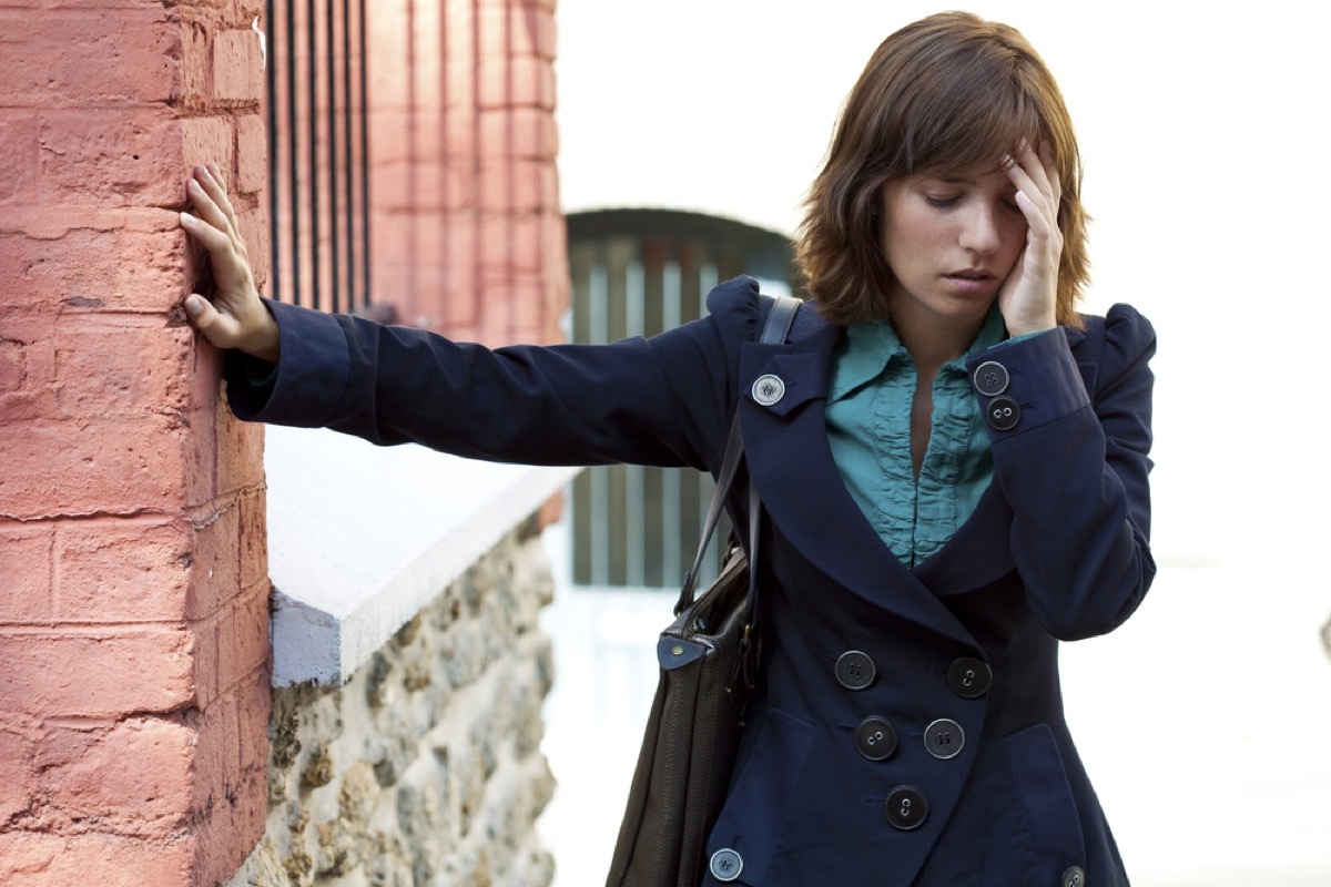 white woman holding the wall and touching her head