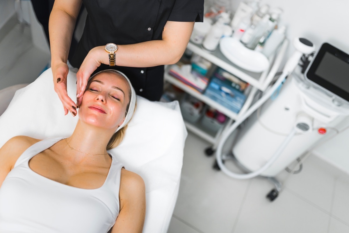 Gentle face massage treatment performed by professional aesthetician. Beauty salon interior. 