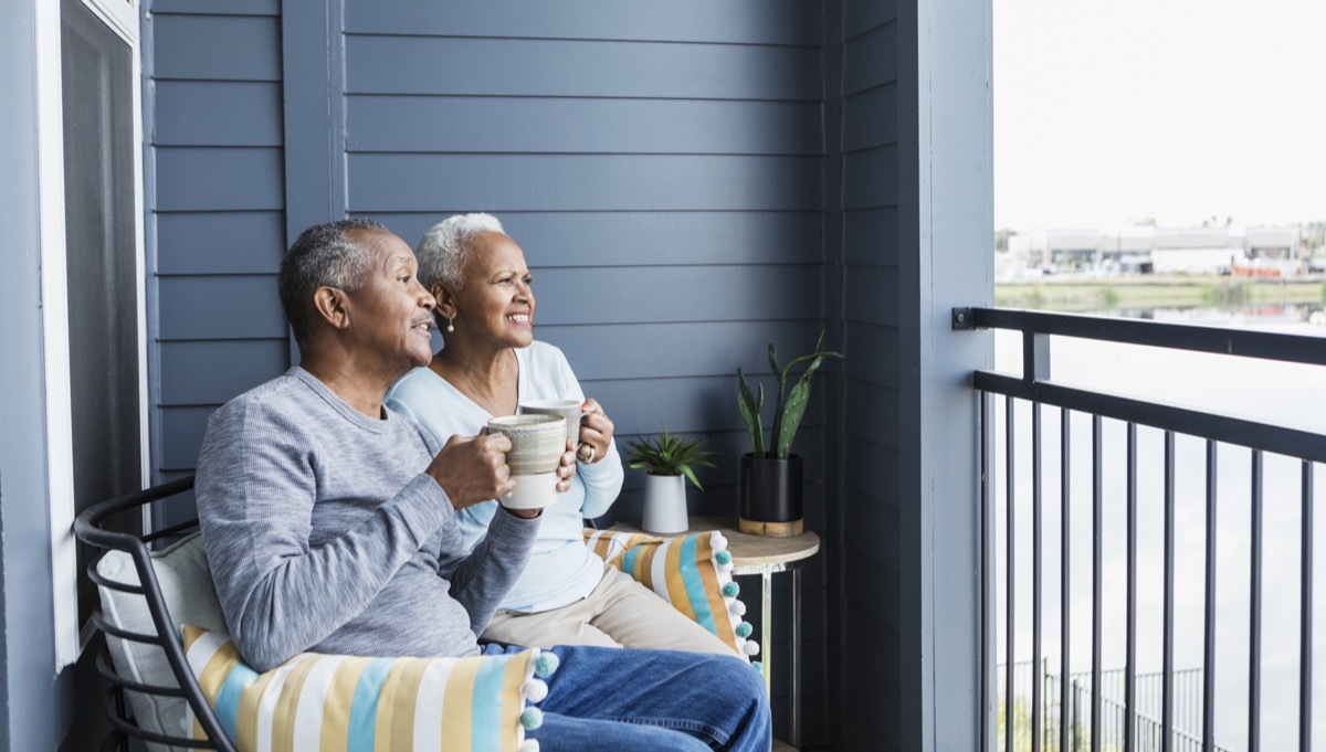 couple sitting side by side on their porch or balcony, drinking coffee. They are looking at something in the distance, squinting to try to figure out what it is.