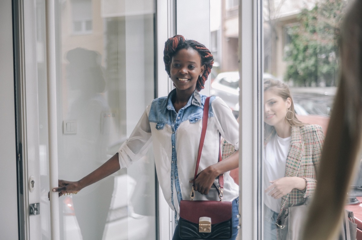 black woman opening the door and entering a store with a white woman standing behind her