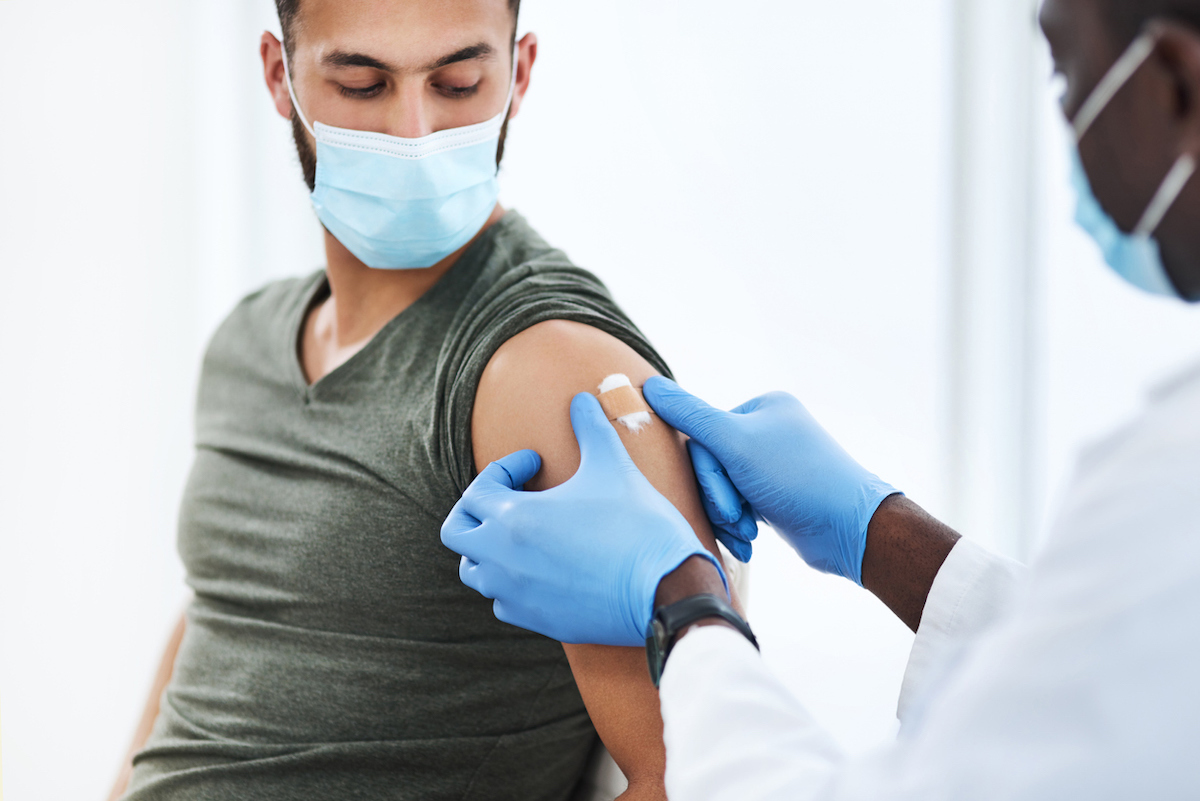 Shot of a doctor applying a band aid after injecting a patient in his arm with COVID vaccine