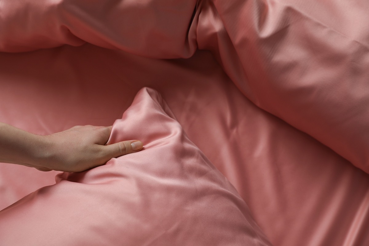 Woman making bed with beautiful pink silk linens, closeup view