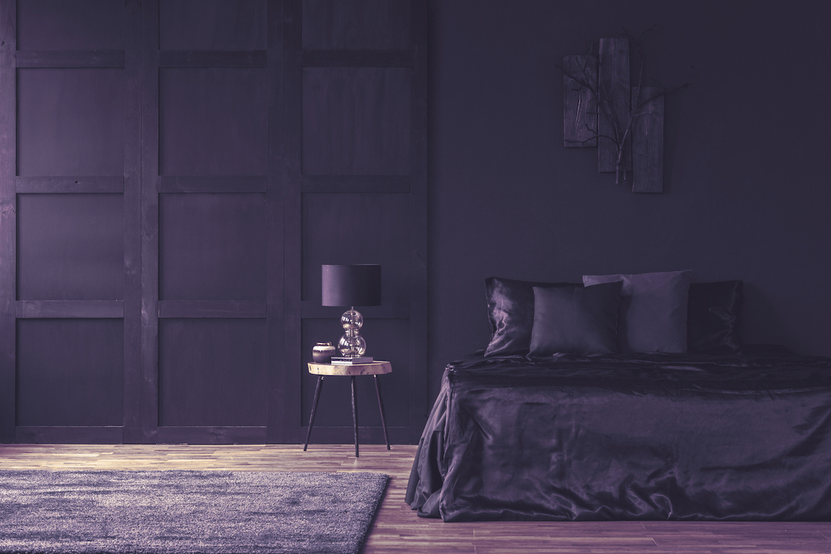 Lamp on wooden table in spacious violet bedroom with matching dark-purple bedding