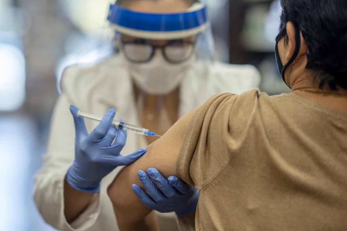 Masked senior woman getting a vaccine while at the pharmacy by a female pharmacist.