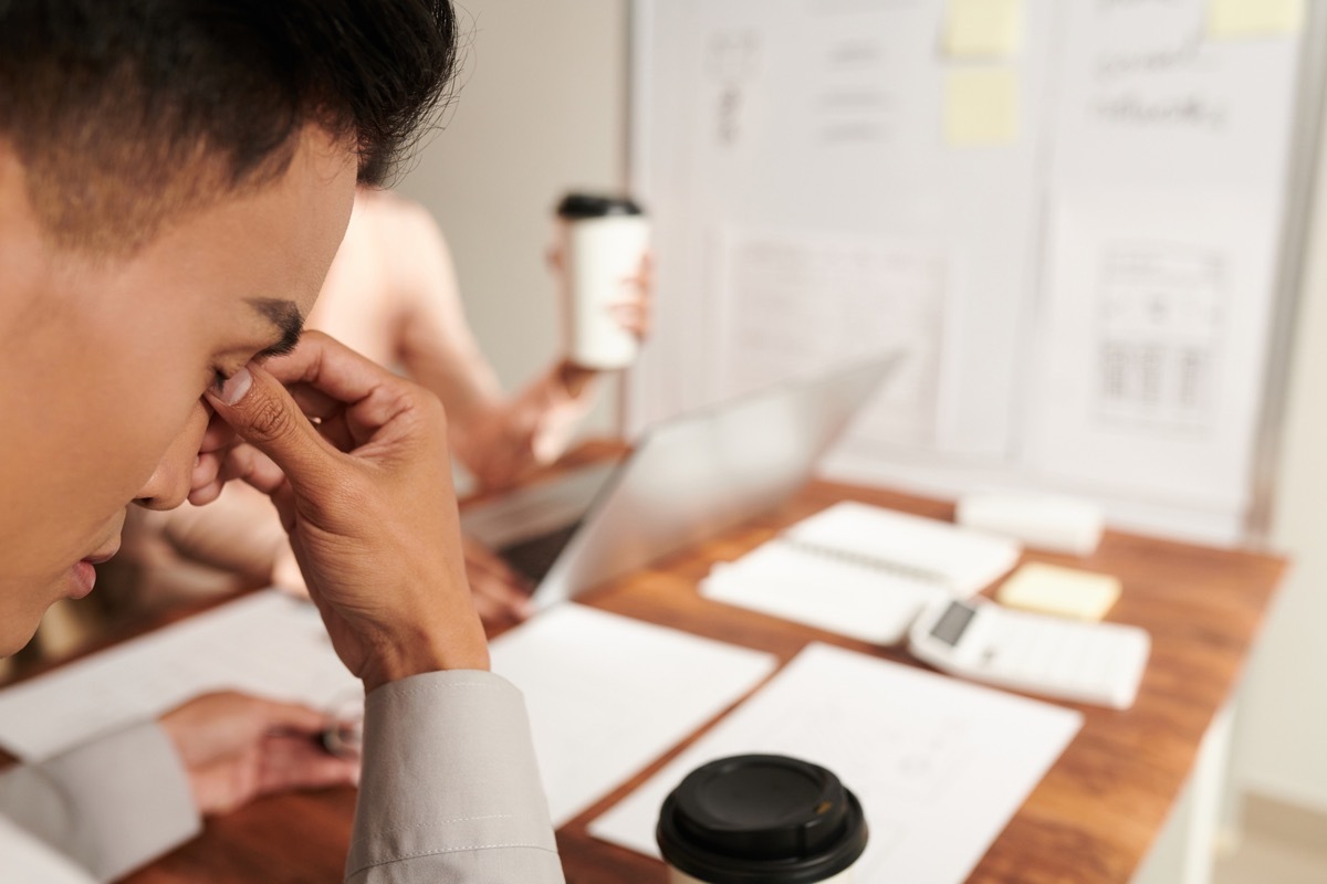 Tired businessman rubbing bridge of his nose after having stressful meeting in office