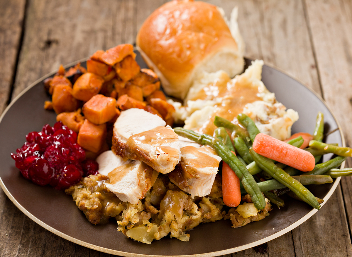 A high angle close up shot of a brown plate containing a bountiful thanksgiving turkey dinner. Shot on a grungy old wooden table