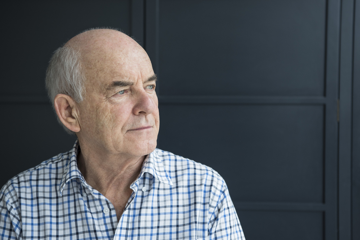 An older man with male pattern baldness looks out a window