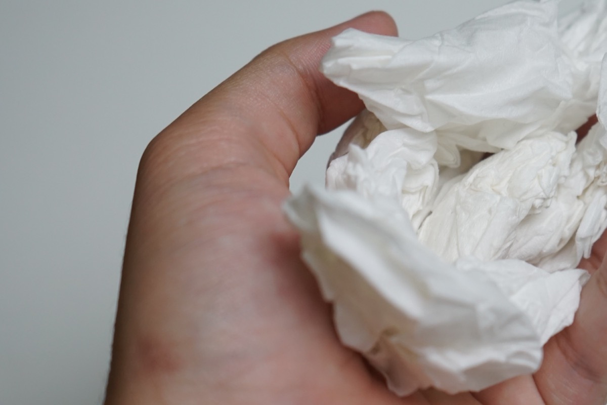 asian hand holding a wad of white tissue crumpled from use, on a white background