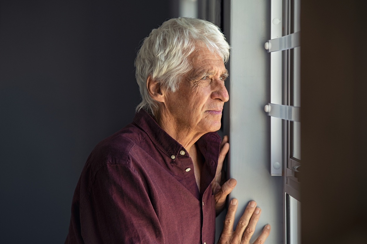 Senior man looking out a window.