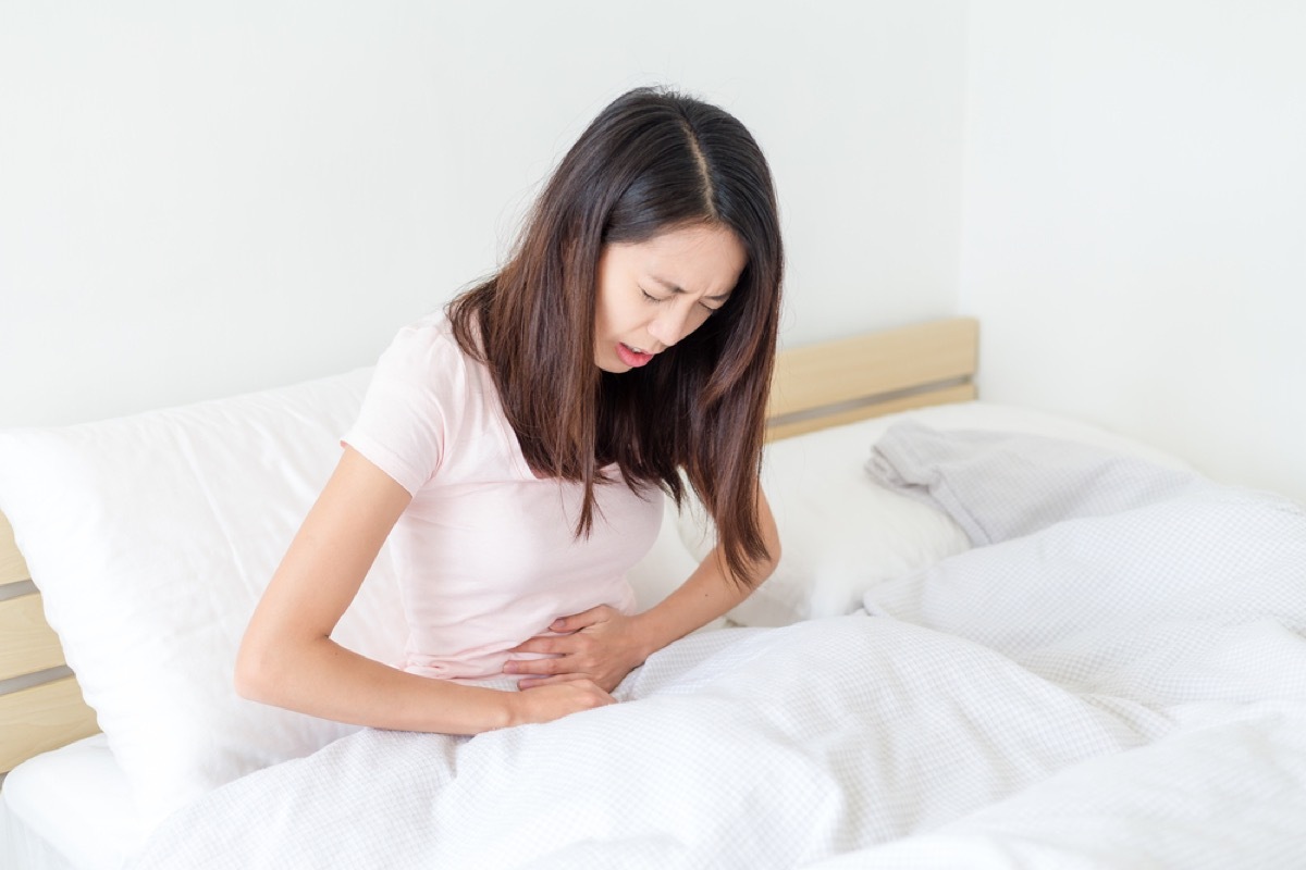 young woman with stomach pain curled over in bed, stomach symptoms