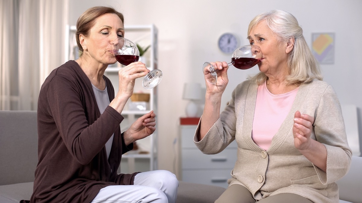 Two elderly women drinking red wine from glasses, friends communication at home