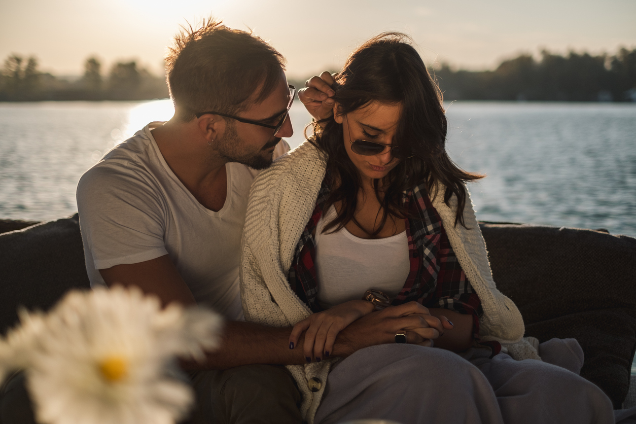 white man trying to console sad white woman sitting by the water