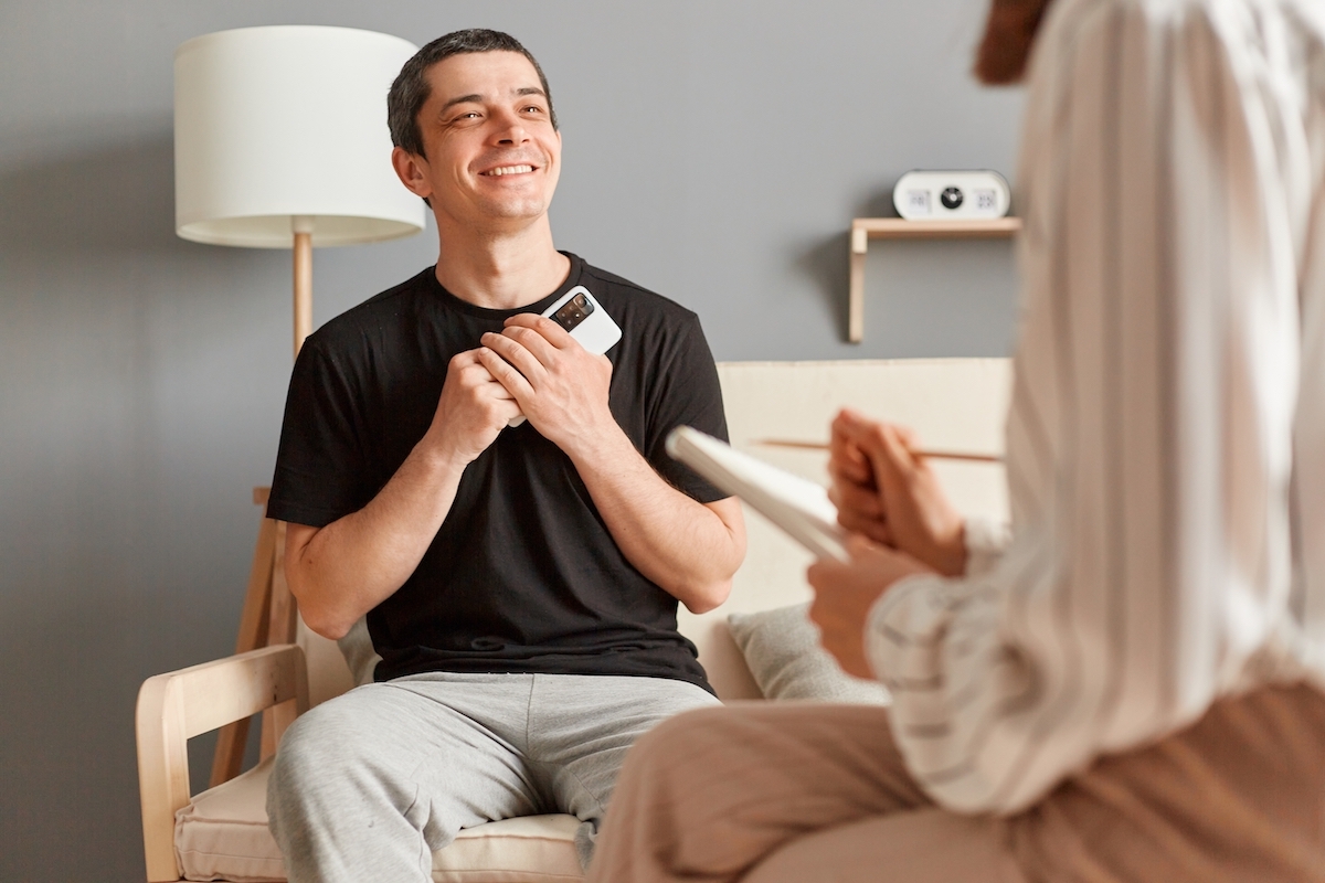 A smiling young man shielding his phone from his therapist.