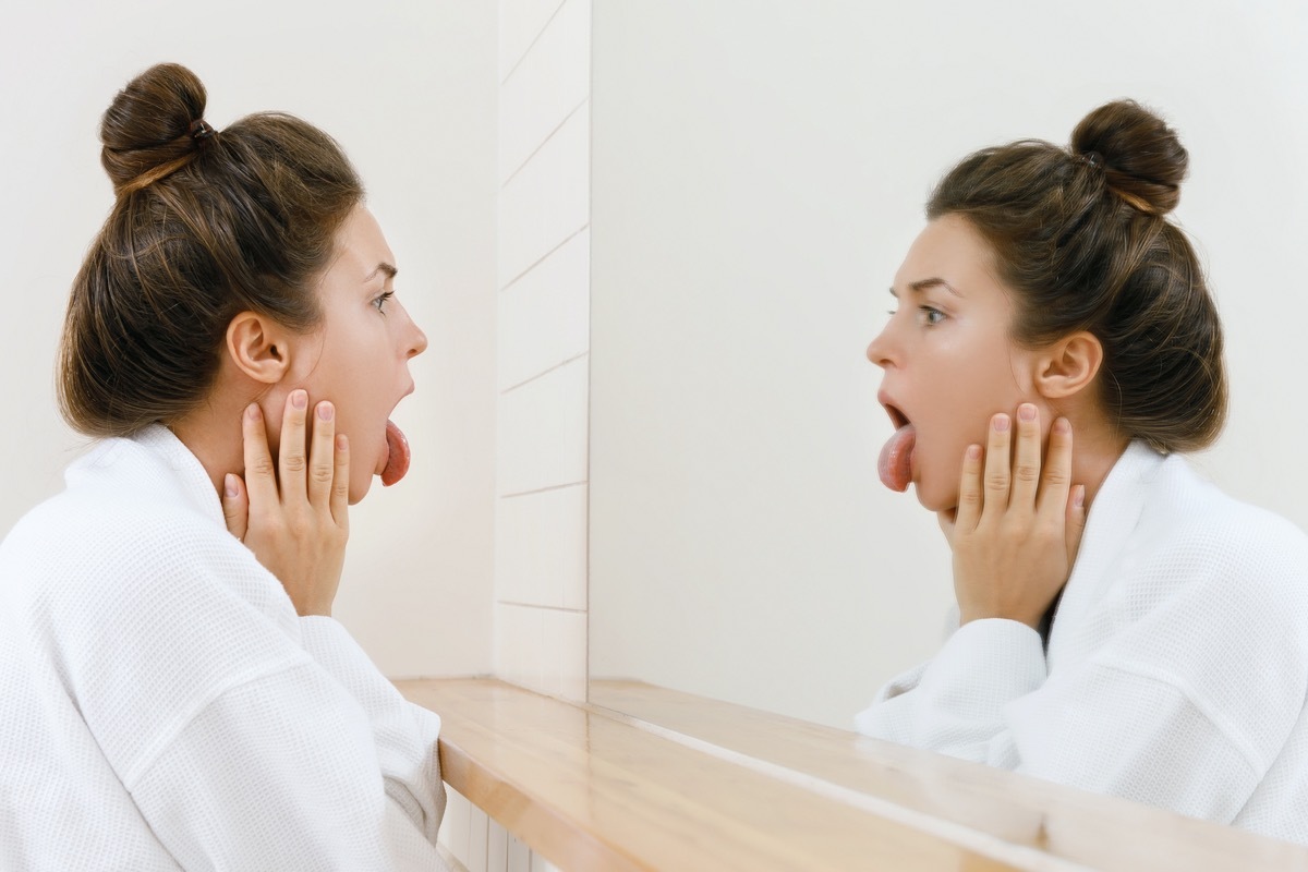 Young woman is looking on her tongue in the mirror