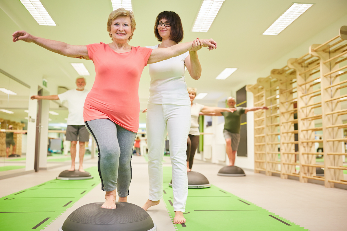 Trainer gives senior help with balance training at the Bosu Ball in the fitness class