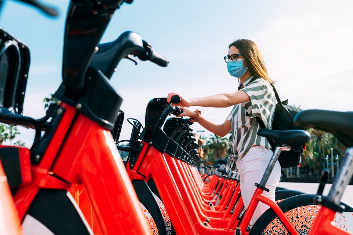 Woman wearing protective face mask taking a rented electric bicycle