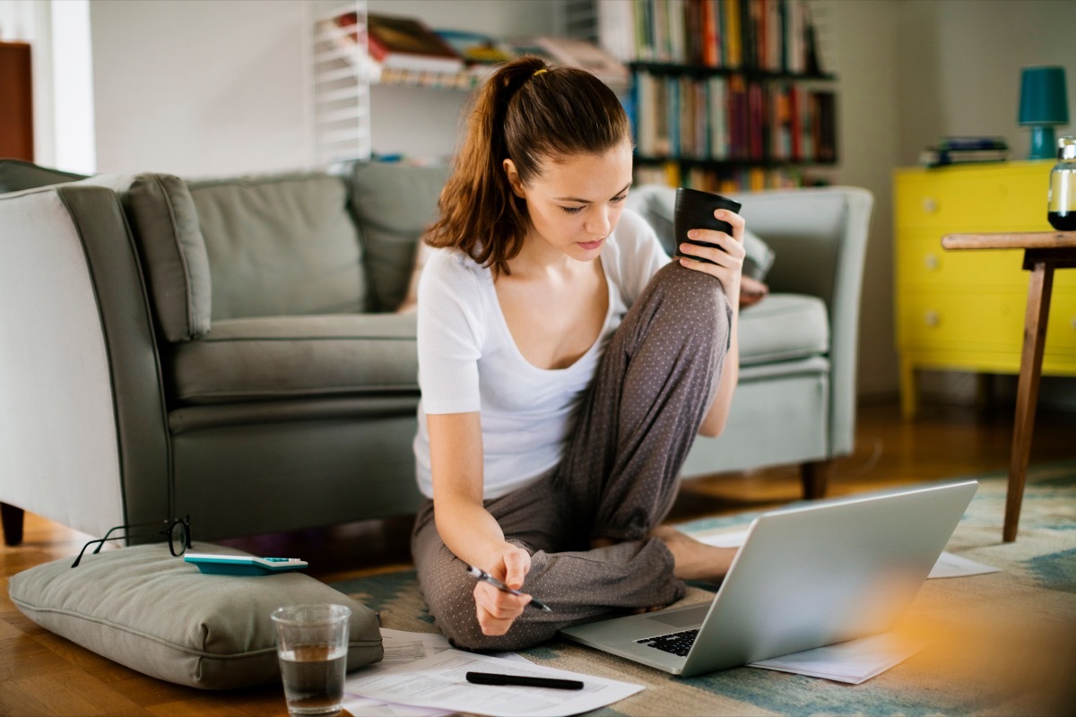 Photo of a young woman sitting on the floor and working on laptop